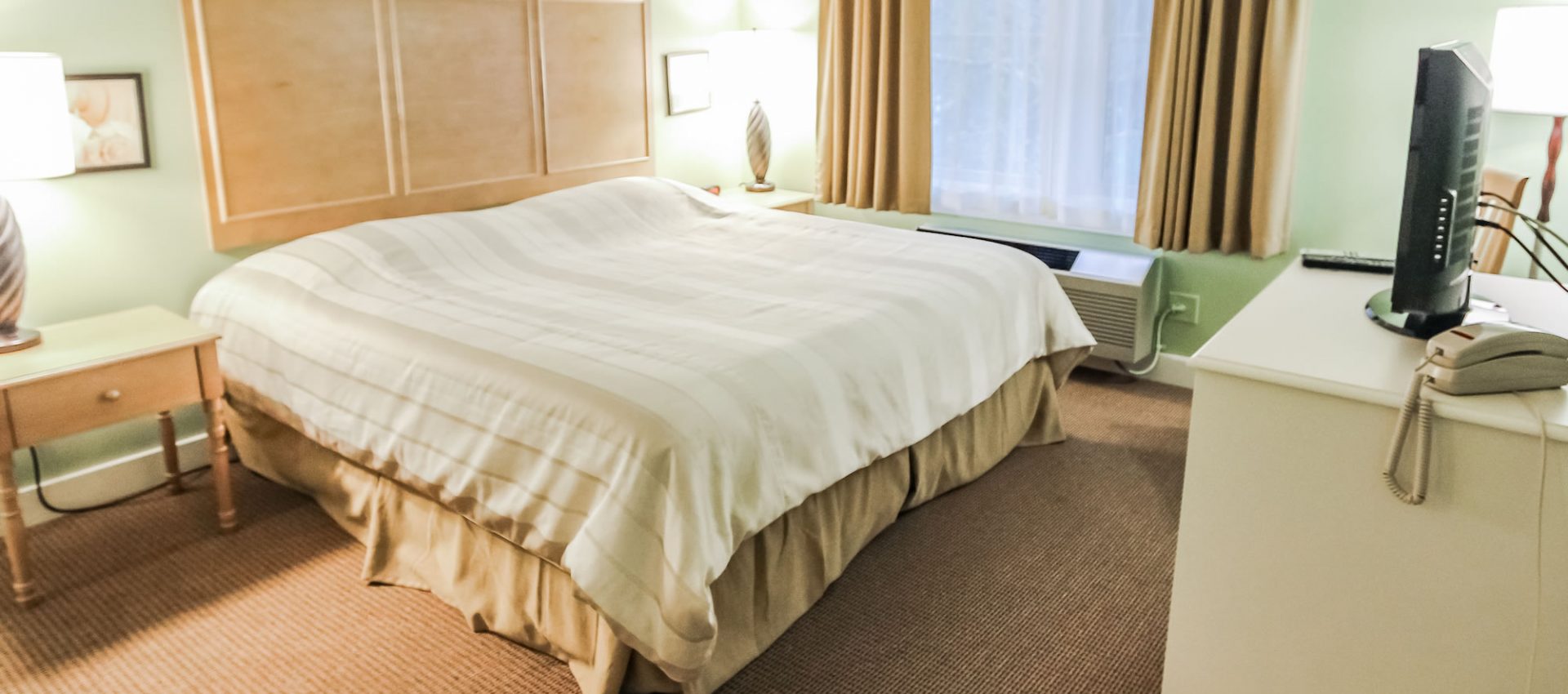 Photo of bedroom with bed, dresser, side tables and television